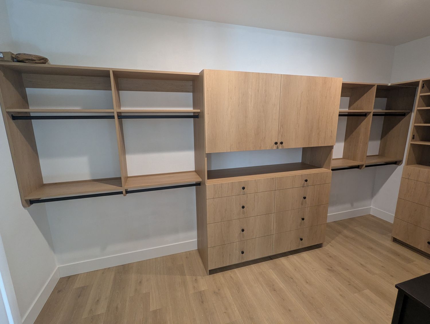 Wood grain walk-in closet with double-door cabinet over a drawer stack and hanging sections on both sides